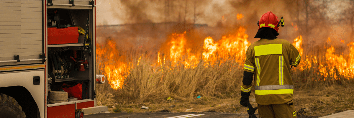 A firetruck and firefighter, with flames burning near a road.